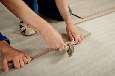 Person installing laminate flooring with a scraper